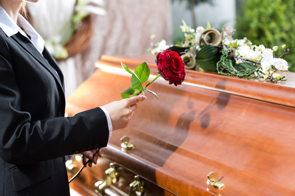 A woman mourning at a funeral with a red rose standing near a casket